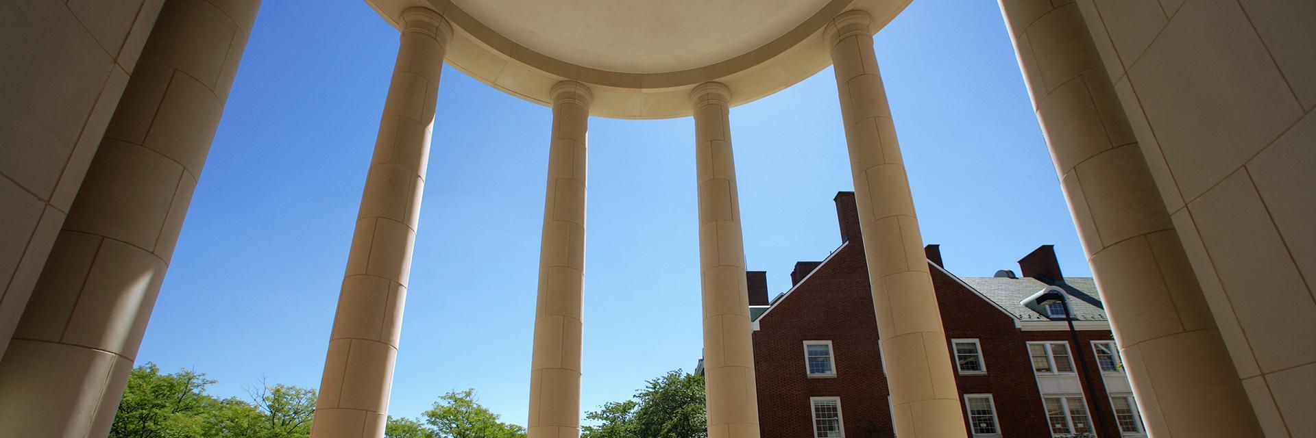 View of a brick building and clear blue sky framed by four large white columns.