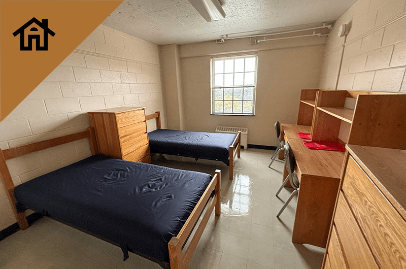 A furnished residence hall room with two twin beds, two desks, and a dresser.