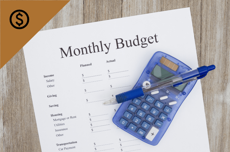 A paper titled "Monthly Budget" is laid out on a table under a blue calculator and pen.