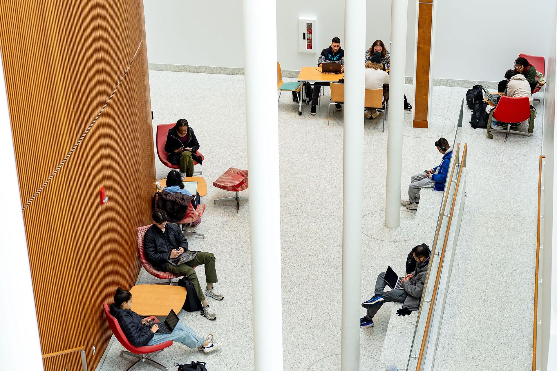 Students studying with laptops in a spacious, modern atrium in the ESJ building.